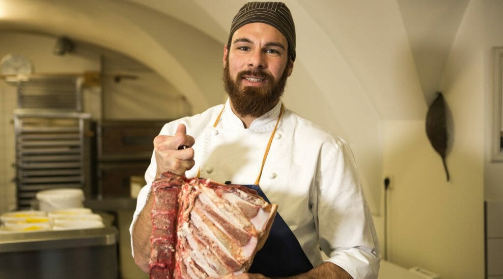 a man standing in a kitchen holding raw red meat