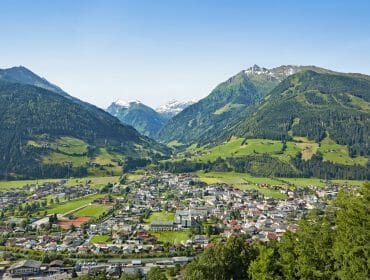 A small town, Mittersill, nestled in a green valley, surrounded by tall forested mountains under a clear blue sky.