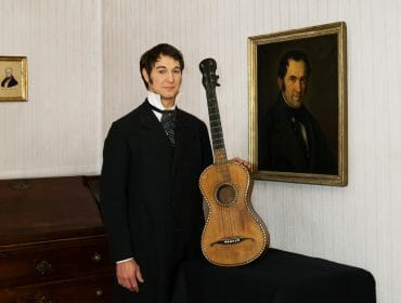 Franz Gruber standing holding his Guitar and posing for the camera