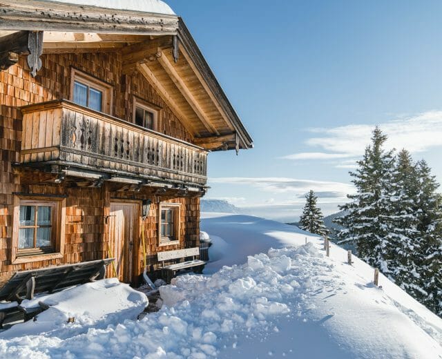snowy hut © SalzburgerLand Tourismus A traditional wooden cabin sits on a snowy hillside with pine trees and a clear blue sky in the background.