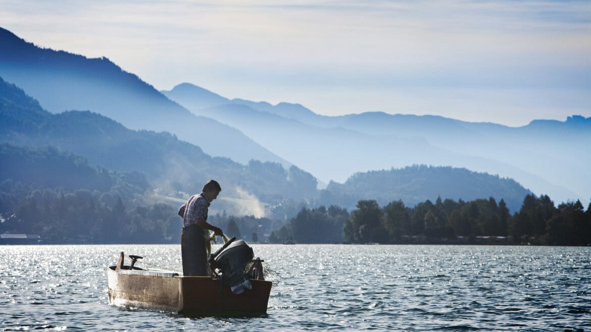 a man in a boat on the water with a mountain in the background