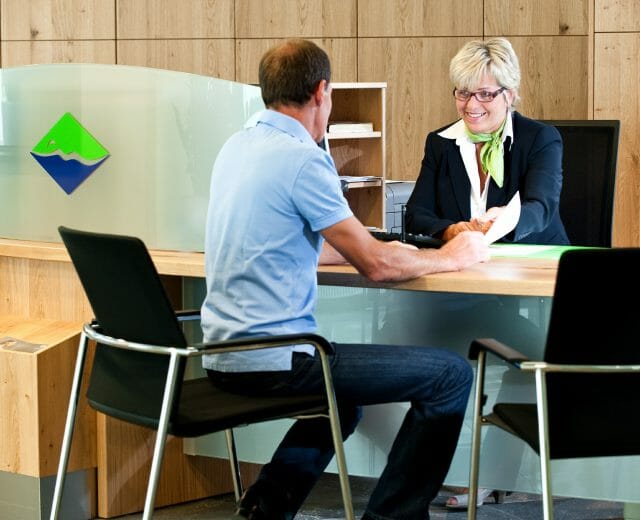 dialyse A man and a woman speak across an office desk; the woman hands him a document and smiles.