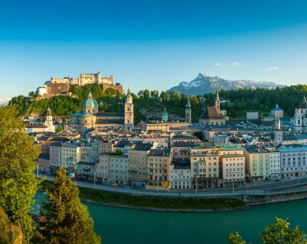 Scenic view of Salzburg, Austria with historic buildings, a fortress, and mountains in the background.
