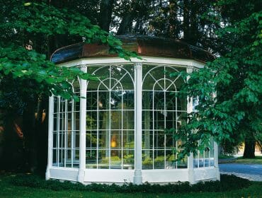 White glass pavilion with a domed roof, like those seen on Sound of Music tours, amid lush green trees and grass.