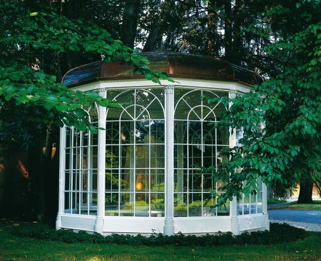 Sound of Music Gazebo in Hellbrunn White glass pavilion with a domed roof, like those seen on Sound of Music tours, amid lush green trees and grass.