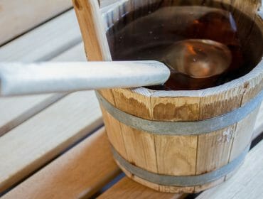 A wooden sauna bucket filled with water and a ladle, placed on a wooden bench.
