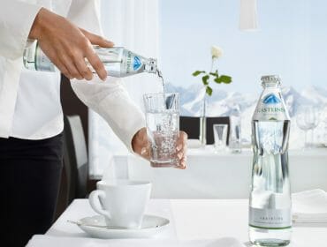 a person filling cup of water from a water bottle on a table