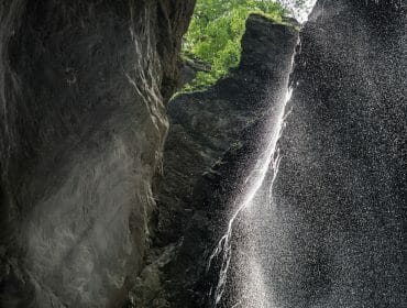 A close-up view of a waterfall cascading in Liechtensteinklamm Gorge, sunlight filtering through green foliage above.