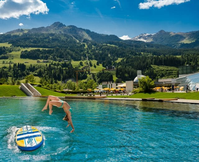 a lady jumping in the water with a mountain in the background