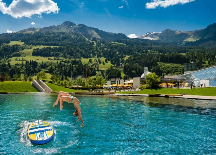 a lady jumping in the water with a mountain in the background