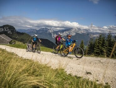 Three cyclists ride on a gravel path in the mountains, exploring scenic parks & trails surrounded by trees.