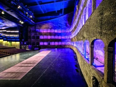 A large theatre stage with stone arches and purple-blue lighting at Felsenreitschule Salzburg.