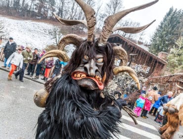 A person in a furry, horned Krampus costume stands before a festive crowd at an outdoor event.