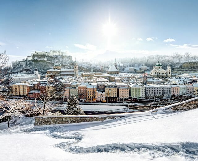 Blick vom Kapuzinerberg auf die Altstadt mit Festung Hohensalzburg Snow-covered cityscape with colourful buildings, a fortress, and the wintry wonders of Salzburgerland in Salzburg.