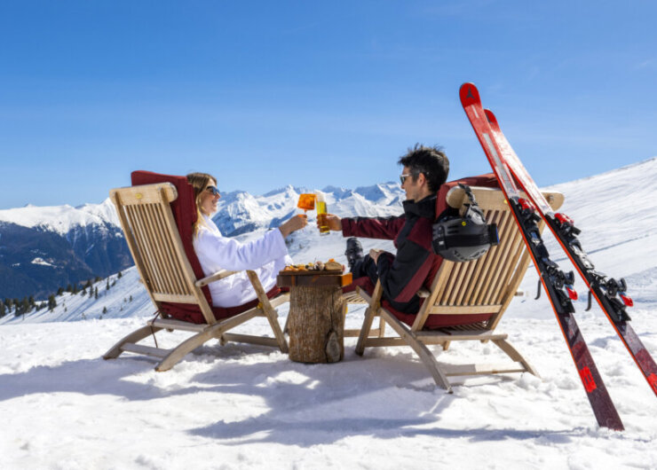 Chillout Skiing (C) Gasteinertal Tourismus GmbH, Max Steinbauer Two people in ski gear toast drinks whilst relaxing in chairs on a snowy mountain with skis nearby.