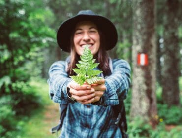 a little girl holding a plant and standing in a forest