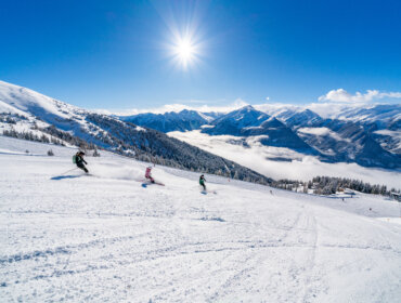 Three skiers on perfect pists - mountains ind the background on a very sunny day