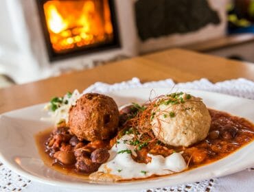 A plate of beans with two dumplings, garnished with herbs, in front of a cosy fireplace.