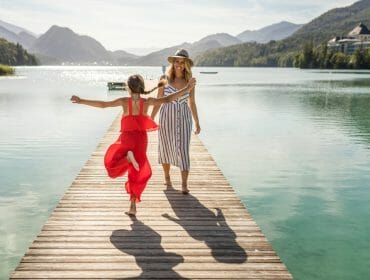 A woman and girl joyfully run on a wooden jetty, showing 10 reasons to love lakes surrounded by mountains.