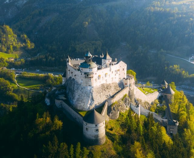 Burg Hohenwerfen Aerial view of a large medieval castle on a hill, surrounded by green trees and mountains.