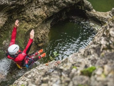 rs1573_2016-09-15-slt-themenshooting-canyoning-salzburgerland-tourismus-michael-groessinger-img_7425-lpr1-1170×658 Person in a helmet and wetsuit jumps into a rocky pool from a height during a canyoning adventure.