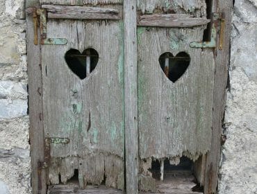 Salzburger-Nachrichten-Heugl-crisis Old, weathered wooden shutters with heart-shaped cut-outs on a rough stone wall.