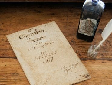 stille-nacht-geschichte Old handwritten document, ink bottle, and quill pen on a wooden desk.