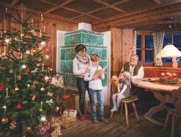Stille Nacht Familie A family celebrates Christmas in a cosy wooden room with a decorated tree and candles on the table.