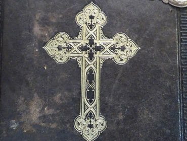 stille-nacht-christian-heugl An ornate gold cross is embossed on the cover of an old black leather book.