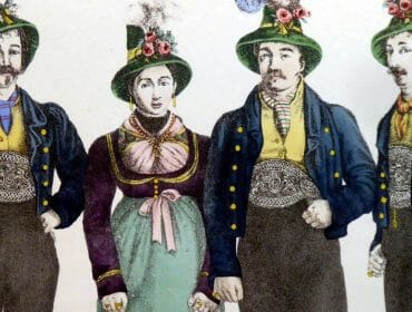 Four people in traditional Austrian clothing, with hats, jackets, and decorative waistbands, standing together.
