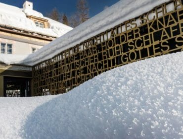 A snow-covered building with decorative metal fencing and icy snowdrifts in bright sunlight.