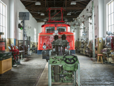 Tauernbahnmuseum in Schwarzach im Pongau A red vintage train inside a museum, surrounded by old machinery and tools on both sides.