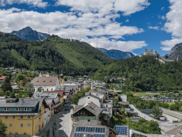A scenic town with colourful houses nestled among green hills and mountains under a partly cloudy sky.