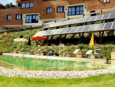 bachgut6-1280×1024-1-1170×658 Solar panels above a natural swimming pool with sun loungers and umbrellas near a modern building.