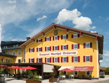 A yellow building with red shutters and Brauerei Gasthof Bräurup written on it, outdoor seating in front.