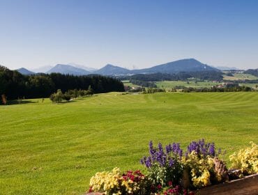 A scenic golf course with mountains in the background and colourful flowers in the foreground.