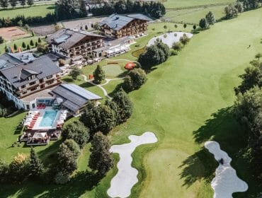 Aerial view of a resort with a pool, surrounding trees, and an adjacent golf course with sand bunkers.