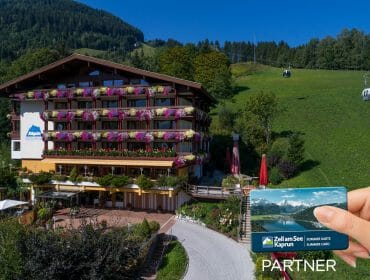 Large alpine hotel with flower balconies, green hills, cable cars, and a hand holding a Zell am See-Kaprun card.