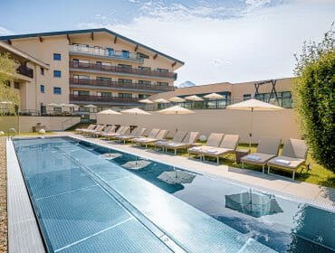 Outdoor swimming pool with loungers and parasols beside a modern hotel building on a sunny day.