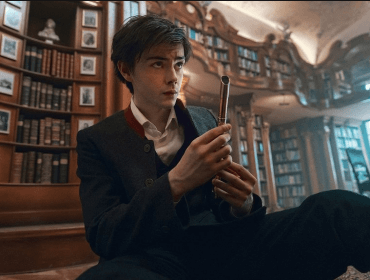 A young person sits on a library floor, holding a metal tube and looking at it thoughtfully.