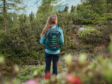 Panorama am Zirbenweg A woman with a rucksack stands on a mountain path, embracing the thrill of the walking week adventure.