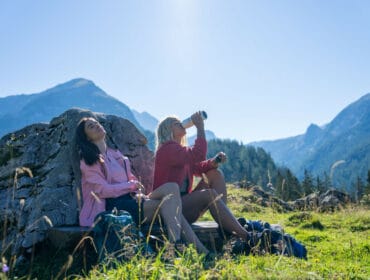 Two women relax by a rock in the mountains, taking the first step into adventure under the sun.