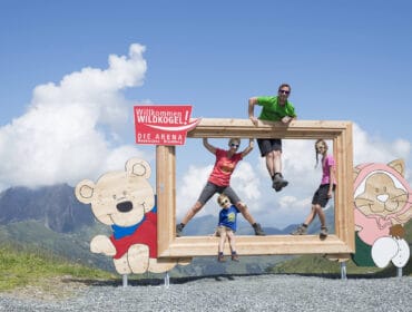 Four people pose in a large wooden picture frame on a mountain with cartoon bear and cat decorations.