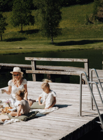 A family enjoys a picnic on a jetty by the lake in sunny SalzburgerLand, guided by their SmartGuide audioguide.