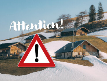 Wooden houses on snowy hillside with Attention! text and red warning sign in foreground.