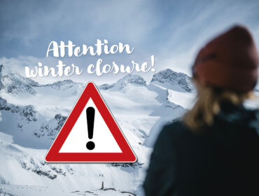 A person faces snowy mountains with a winter closure warning and exclamation mark sign in view.