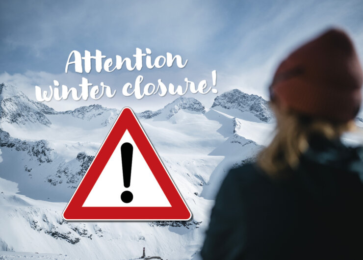 A person faces snowy mountains with a winter closure warning and exclamation mark sign in view.