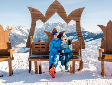 couple sitting on a wooden Throne with mountains in the backround