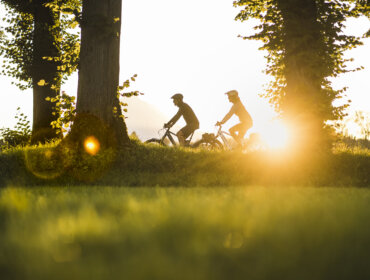 Two people ride bicycles through a grassy park at sunset, echoing the charm of the Alpe Adria Cycle Path.