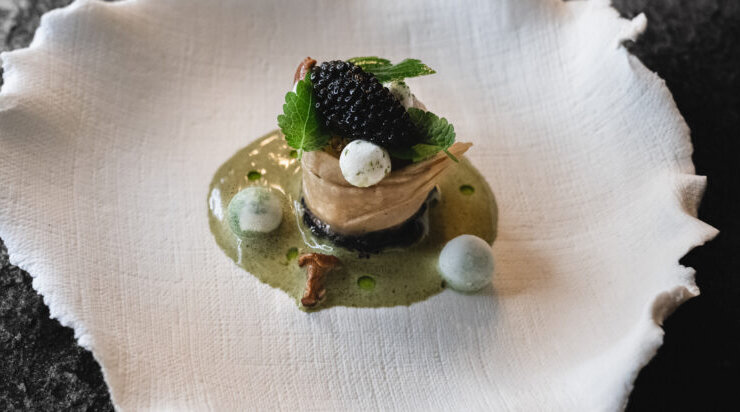 (c) Mario Stockhausen A gourmet dish with caviar, greens, and foam on a textured white plate against a dark background.